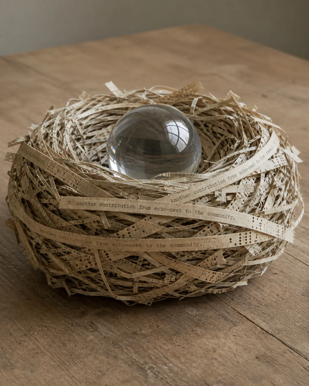 Artist interpretation of echo-nest as a grapefruit-sized nest woven from old paper, ticker tape and punch cards around a clear glass sphere