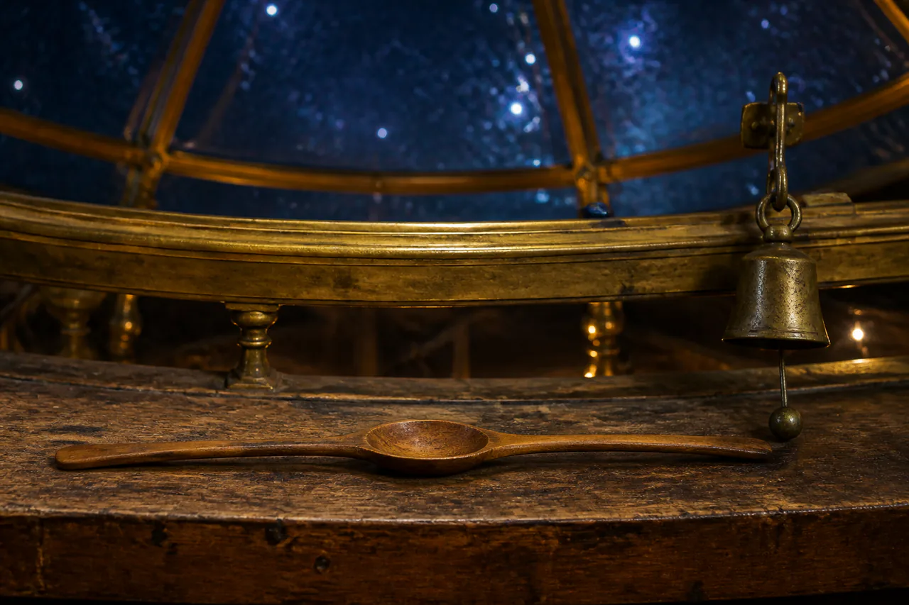 One continuous wooden spoon with a central bowl and two handles beside a small brass chime