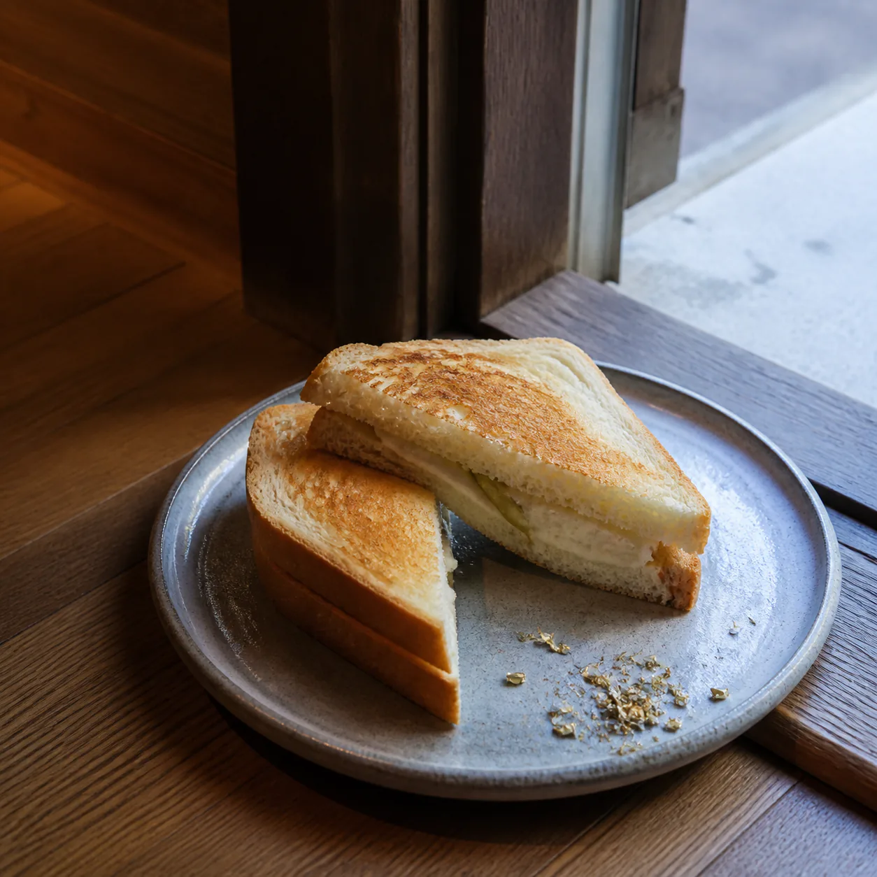 A diagonally cut pale toasted sandwich at an open doorway with a thin hinge-like layer and decorative brass-coloured shavings beside it